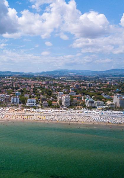 Spiaggia affollata con ombrelloni e mare limpido, città sullo sfondo.