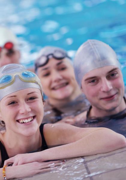 Gruppo di nuotatori sorridenti in piscina con cuffie e occhialini.