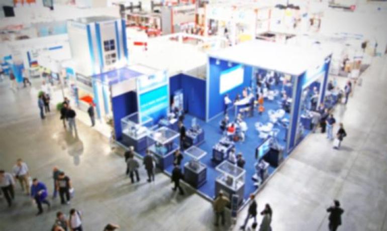 Fiera commerciale con stand blu e visitatori che passeggiano.