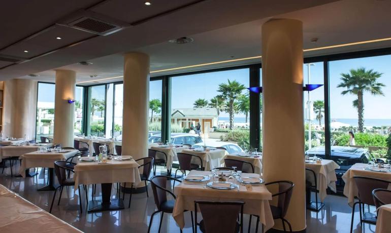 Ristorante elegante con vista mare, tavoli apparecchiati e palme.