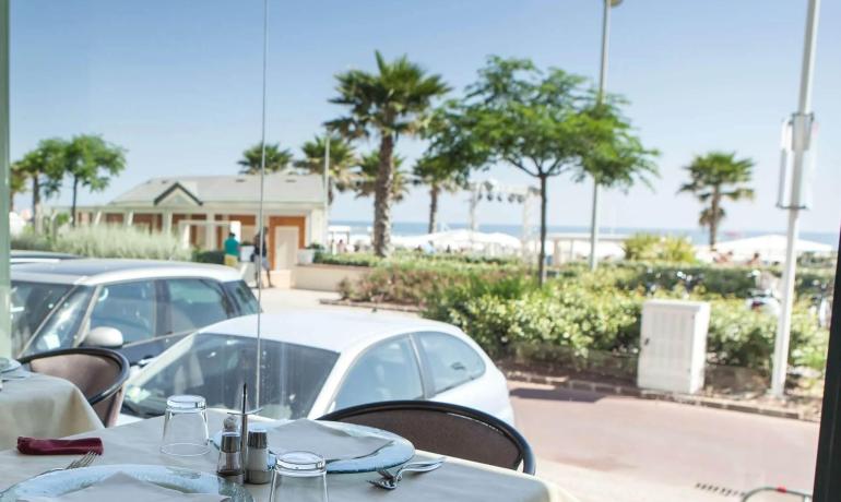 Ristorante con vista mare, palme e auto parcheggiate.