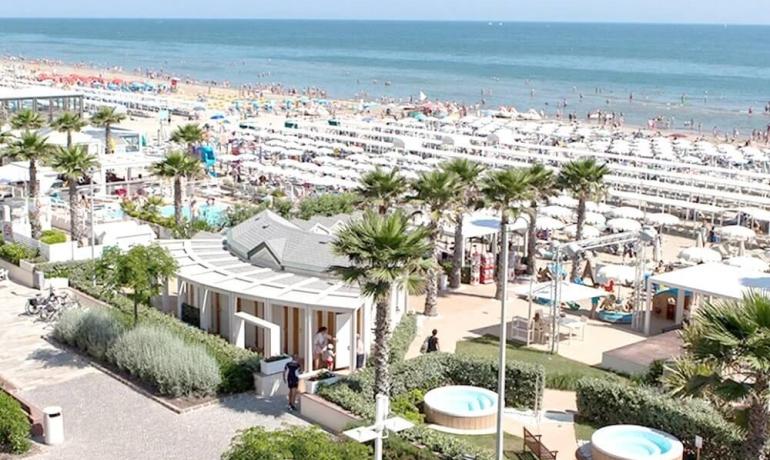 Spiaggia affollata con ombrelloni e palme, vista mare.