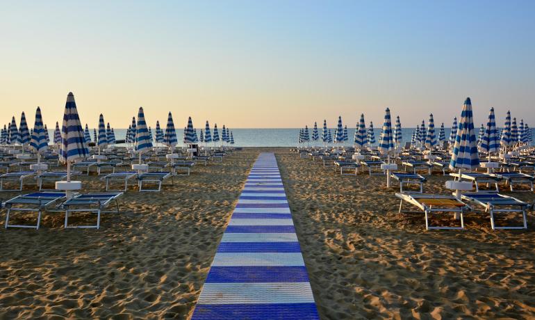 Spiaggia con ombrelloni blu e bianchi al tramonto.