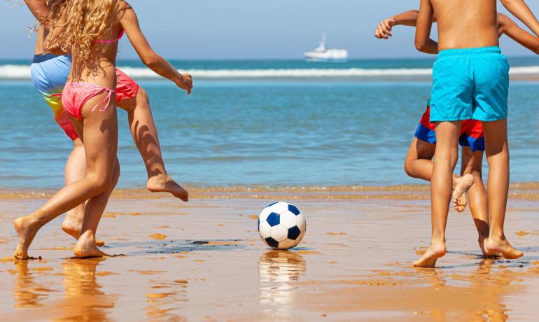 Bambini giocano a calcio sulla spiaggia, giornata soleggiata.