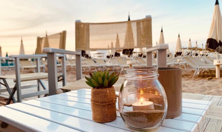 Tavolo sulla spiaggia con candela e pianta al tramonto.