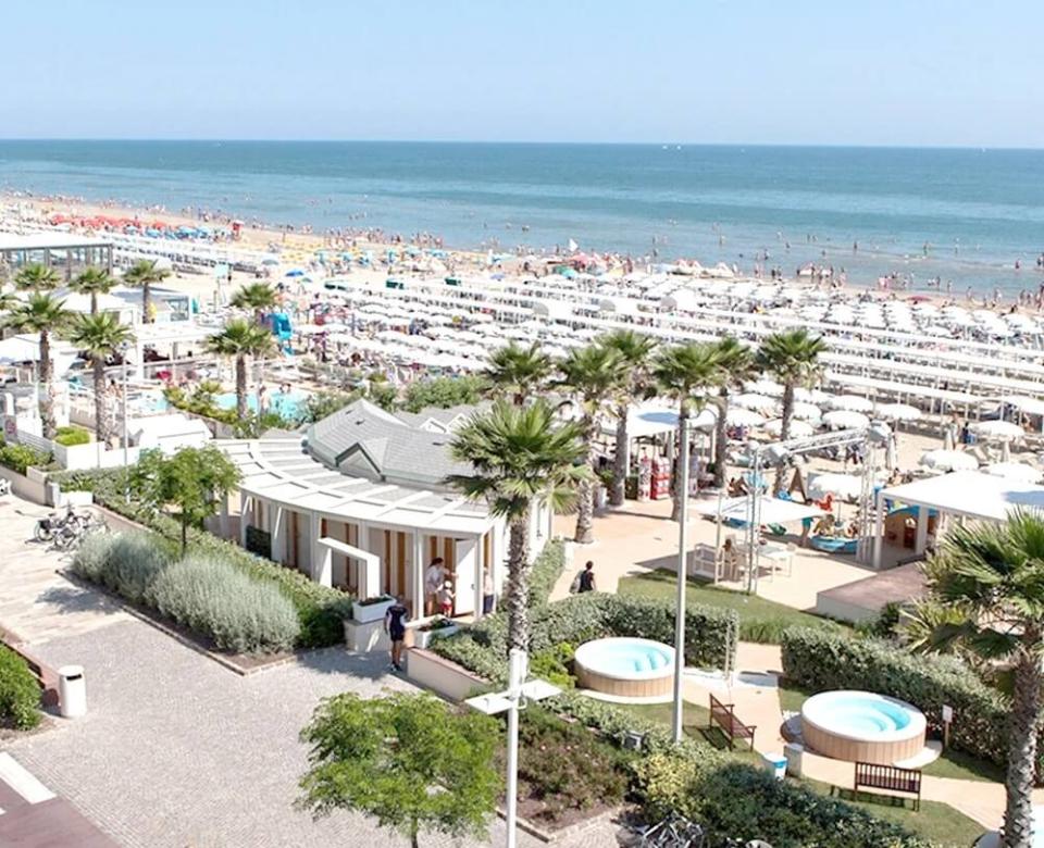 Spiaggia affollata con ombrelloni, palme e strutture vicino al mare.